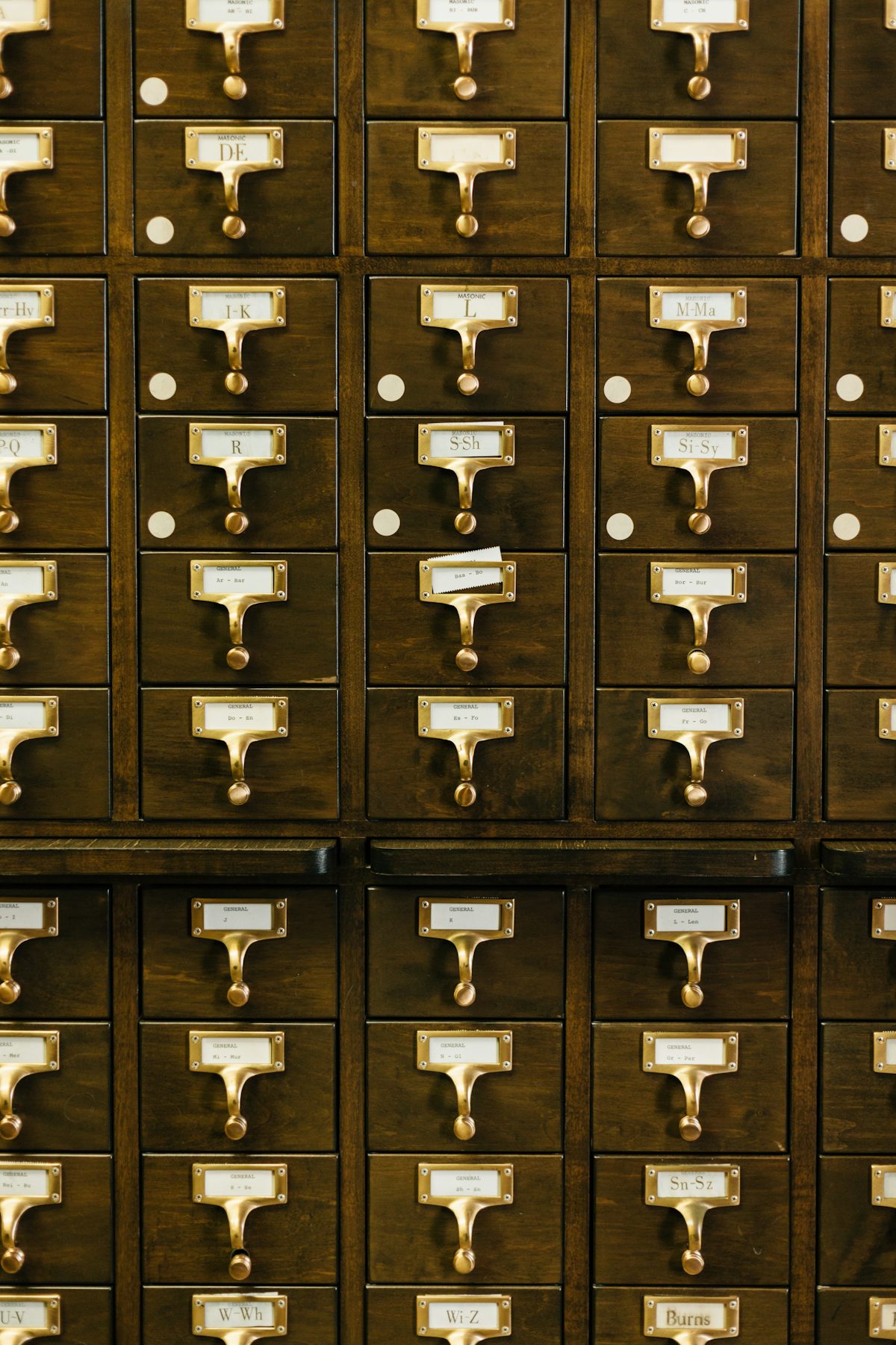 A wall of labeled wooden library card catalog drawers with brass handles